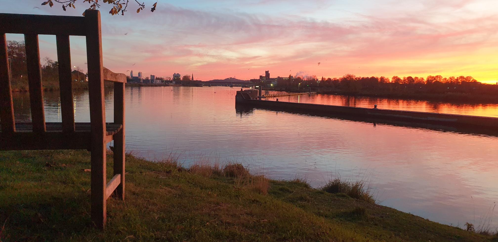 Bankje aan de Maas bij zonsondergang met de skyline van Maastricht