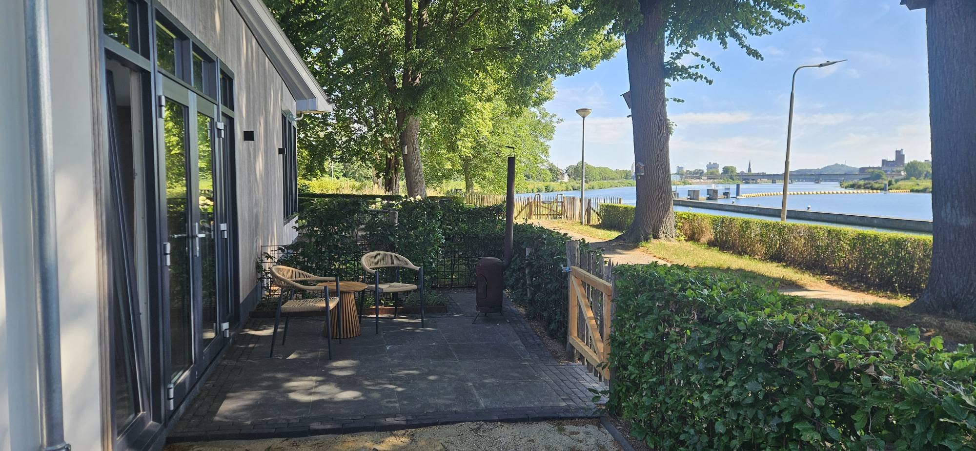 Terras met zithoek onder de bomen aan de Maas